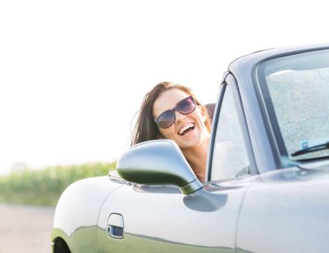 Woman in the passenger seat of a convertible enjoying a summer road trip