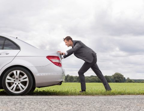 A man in a suit pushing his broken down car on the road.