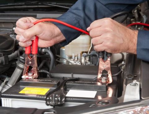 mechanic charging a cars battery with jumper cables